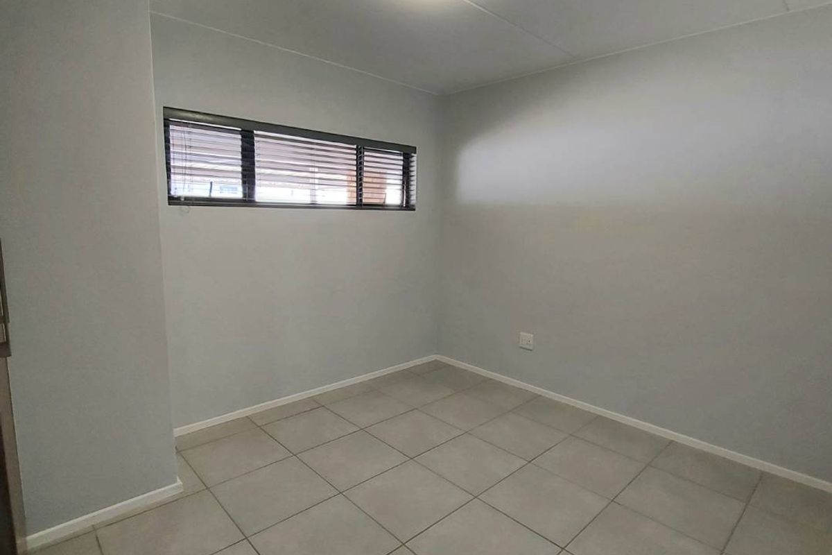 A clean, empty bedroom featuring neutral grey walls, tiled flooring, and a horizontal window with fitted blinds.
