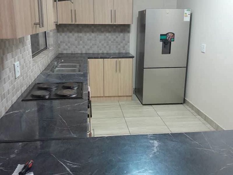 Modern kitchen featuring light wood cabinetry, dark marble-effect countertops, tiled backsplash, and integrated electric hob with extractor fan.