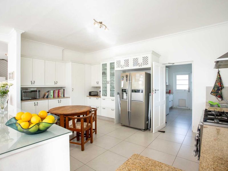 Spacious kitchen featuring white built-in cabinetry, granite countertops, gas hob, and tiled flooring, with an adjacent scullery area visible.