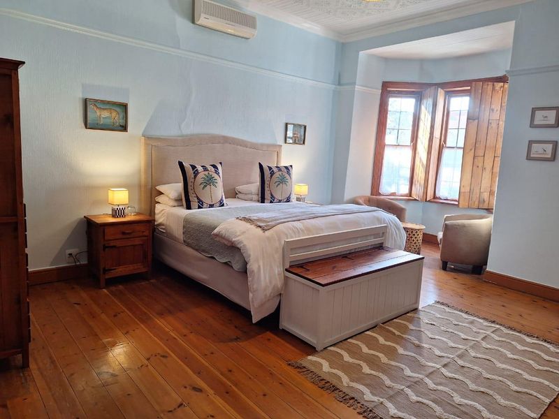 Spacious bedroom featuring original hardwood flooring, a bay window with timber shutters, decorative ceiling details, and a wall-mounted air conditioning unit.