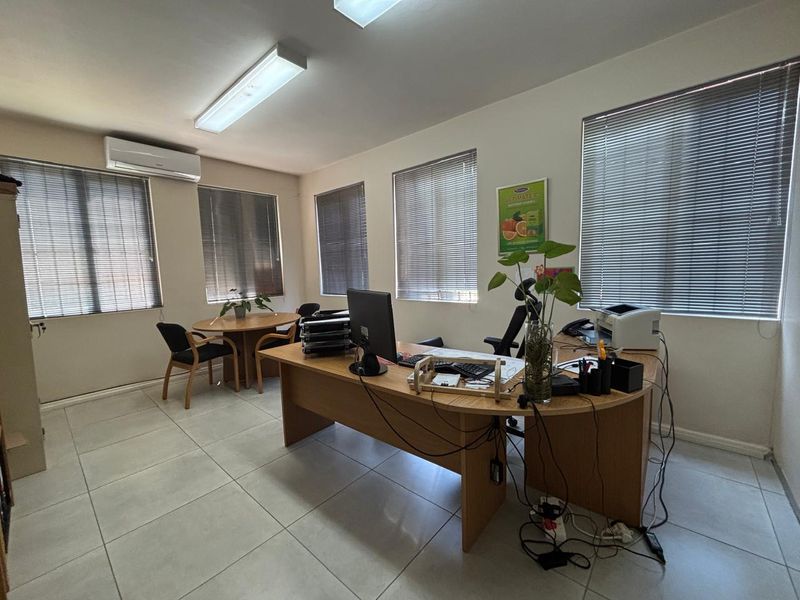 A functional office space featuring tiled flooring, multiple windows with venetian blinds, and a wall-mounted air conditioning unit.
