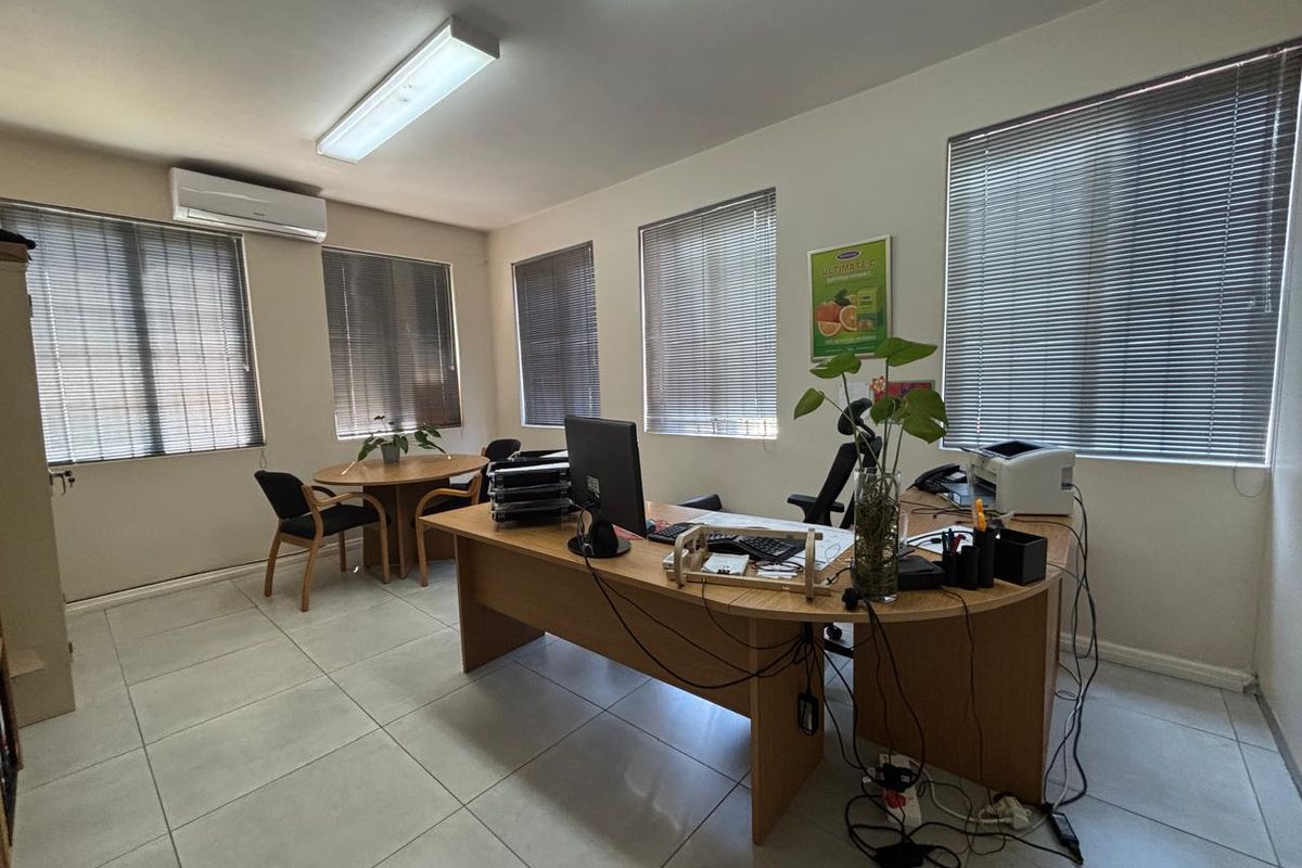 A functional office space featuring tiled flooring, multiple windows with venetian blinds, and a wall-mounted air conditioning unit.