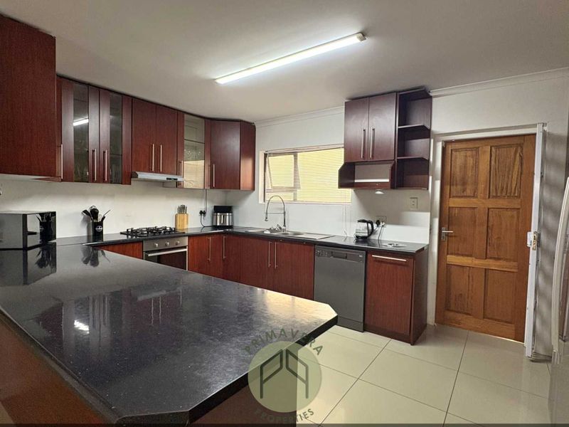 A functional kitchen featuring dark wood cabinetry, black granite countertops, built-in oven, gas hob, and tiled flooring.