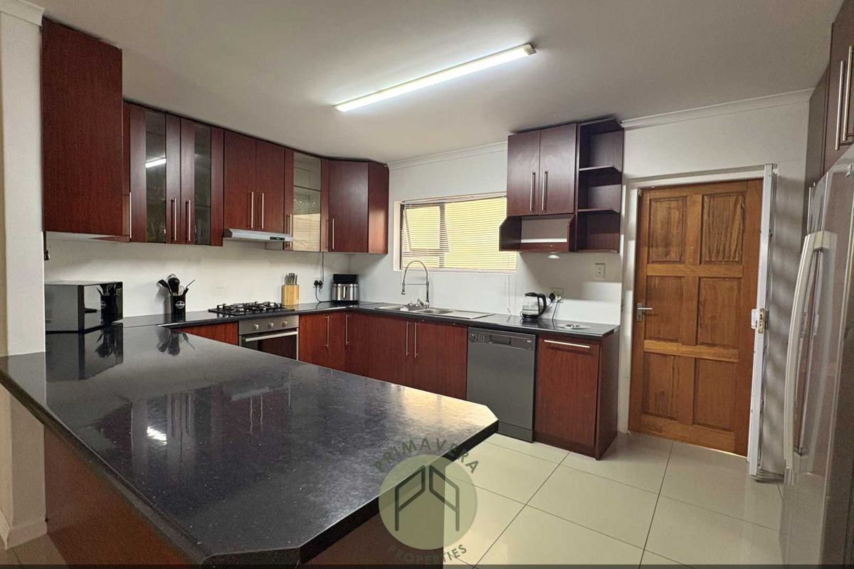 A functional kitchen featuring dark wood cabinetry, black granite countertops, built-in oven, gas hob, and tiled flooring.