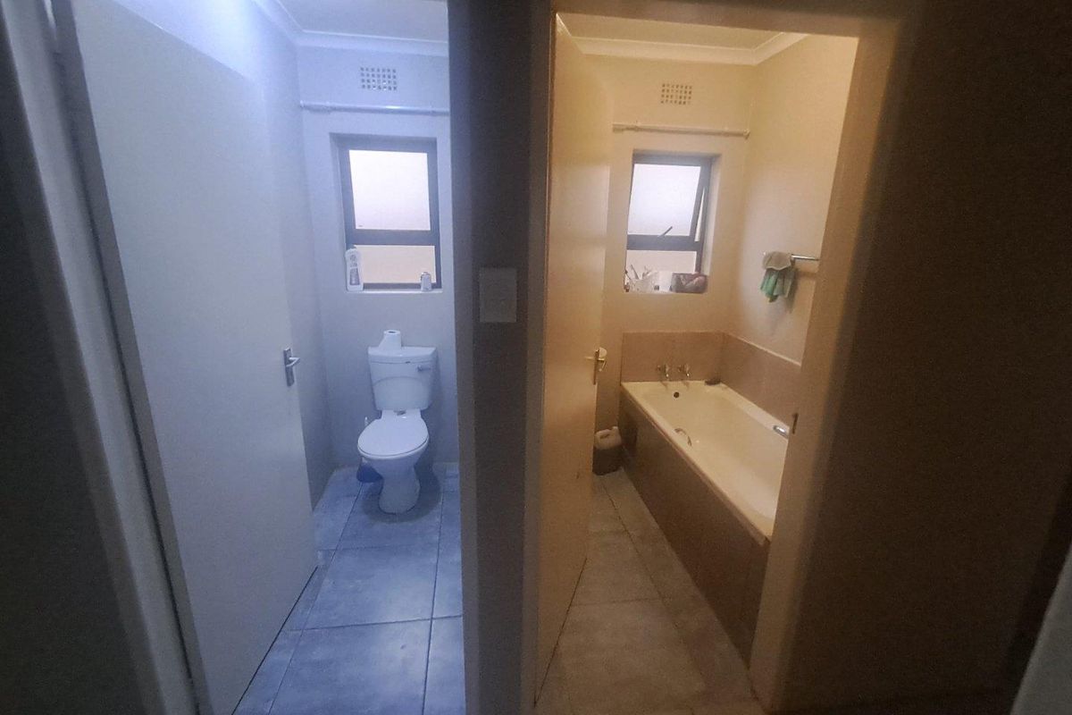 A split-view bathroom featuring a separate toilet area and a bathroom with a built-in bathtub and tiled flooring.