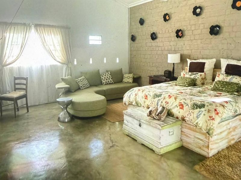 Spacious bedroom featuring a rustic exposed brick feature wall, polished concrete flooring, and a vaulted ceiling, offering a unique farm-style aesthetic.