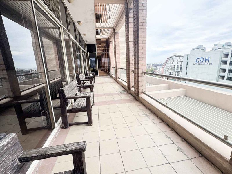 A spacious covered balcony featuring tiled flooring, brick structural pillars, and metal railings, offering an outdoor extension to the office space.