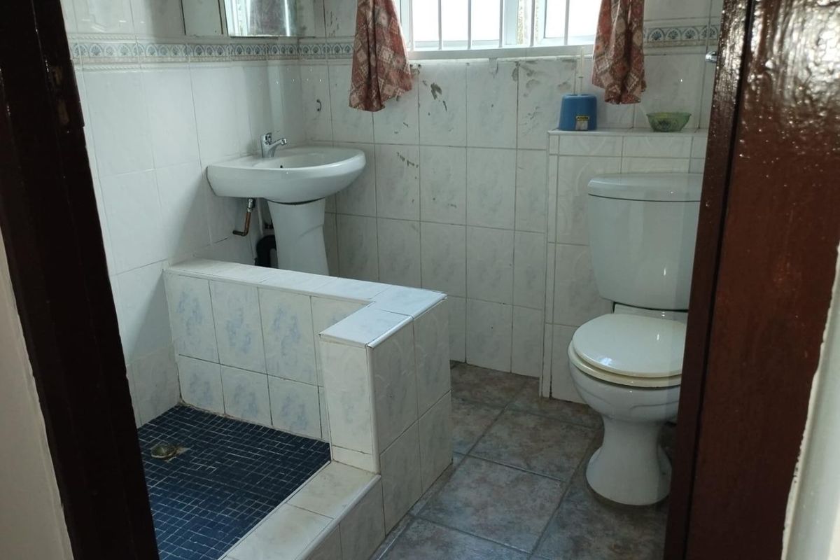A functional bathroom featuring a pedestal sink, toilet, and a tiled shower enclosure with a window providing natural light.