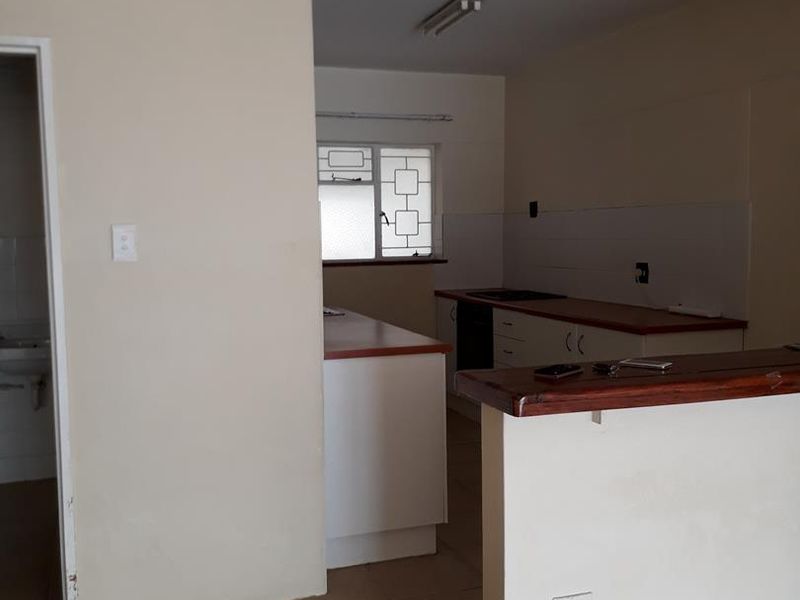 An empty kitchen featuring built-in cabinetry, laminate countertops, and a breakfast bar, with a mix of tiled and parquet flooring.