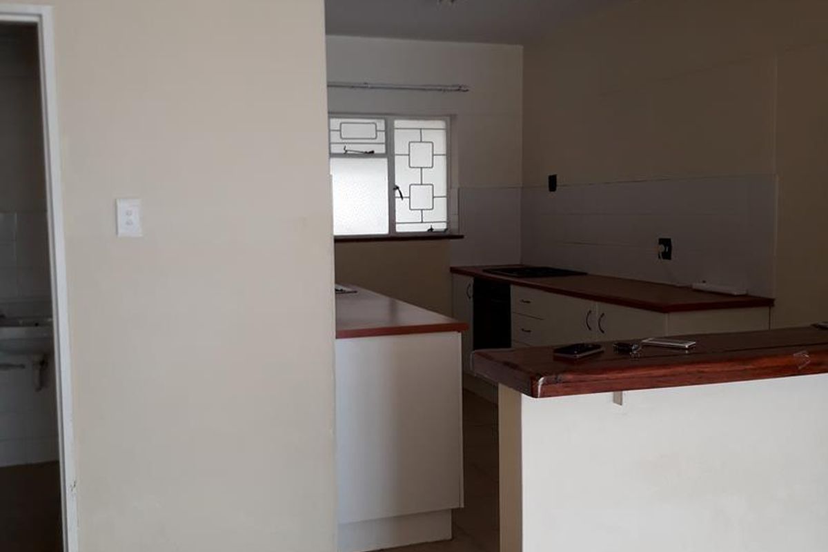 An empty kitchen featuring built-in cabinetry, laminate countertops, and a breakfast bar, with a mix of tiled and parquet flooring.