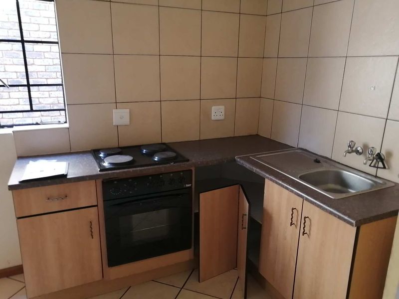 A compact kitchen featuring built-in cabinetry, an electric oven and hob, stainless steel sink, and tiled splashbacks.