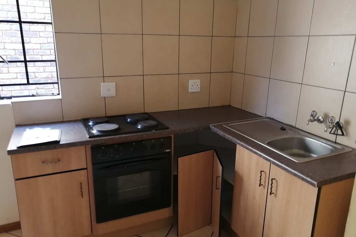 A compact kitchen featuring built-in cabinetry, an electric oven and hob, stainless steel sink, and tiled splashbacks.