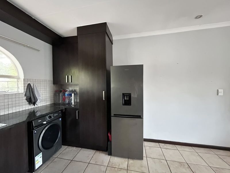 A functional laundry area featuring dark built-in cabinetry, granite countertops, tiled backsplash, and tiled flooring with an arched window providing natural light.