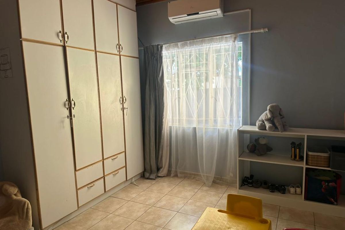 A bedroom featuring built-in floor-to-ceiling cabinetry, tiled flooring, and a wall-mounted air conditioning unit.