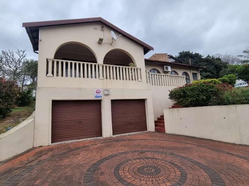 Front elevation of a double-story house featuring a paved driveway, double garage with roller doors, and an upper-level covered balcony.