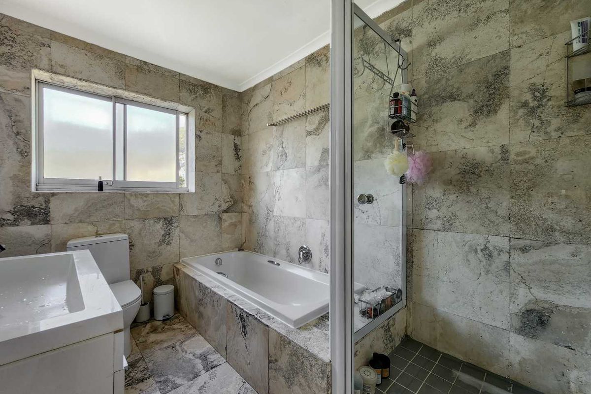A functional bathroom featuring a built-in bathtub, separate glass-enclosed shower, tiled finishes, and a vanity basin with a window for natural light.