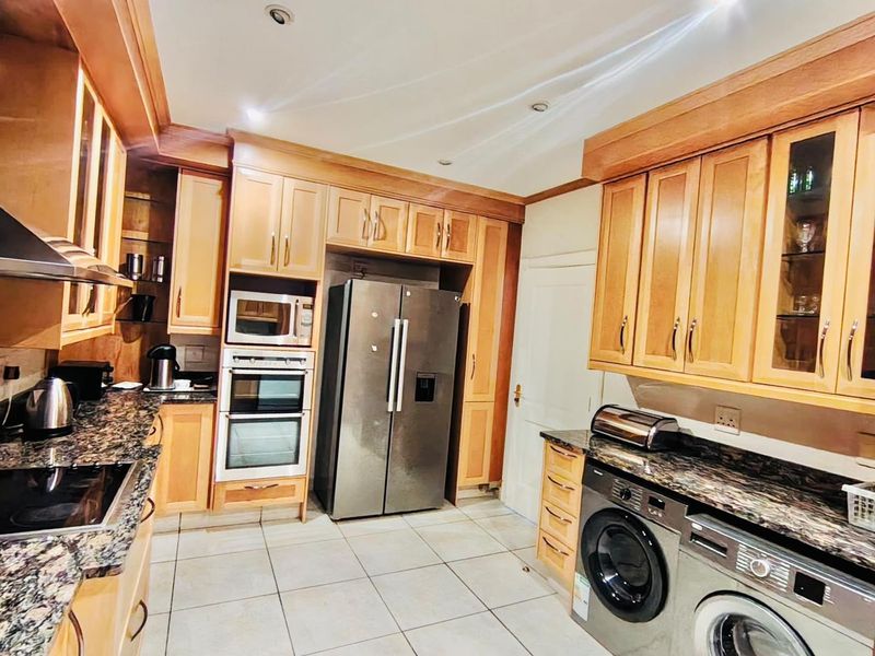 A functional kitchen featuring granite countertops, wooden cabinetry, built-in oven, microwave, and integrated laundry appliances with tiled flooring and recessed lighting.