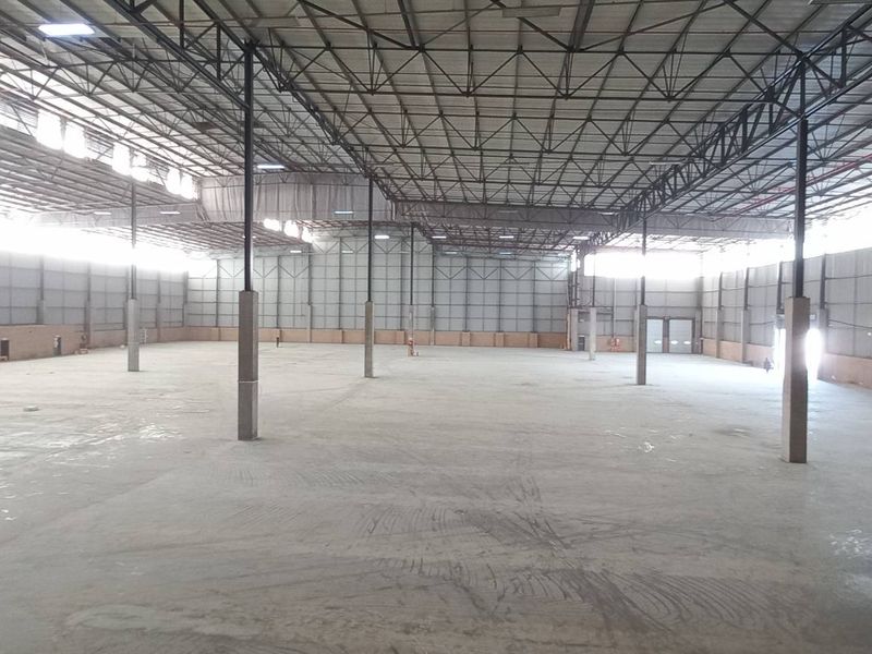 Expansive industrial warehouse space featuring high steel truss ceilings, concrete flooring, and robust steel support columns, suitable for large-scale storage or manufacturing operations.