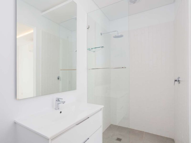 Modern bathroom featuring a sleek white vanity, large wall mirror, and a spacious walk-in shower with a glass screen and rain shower head.