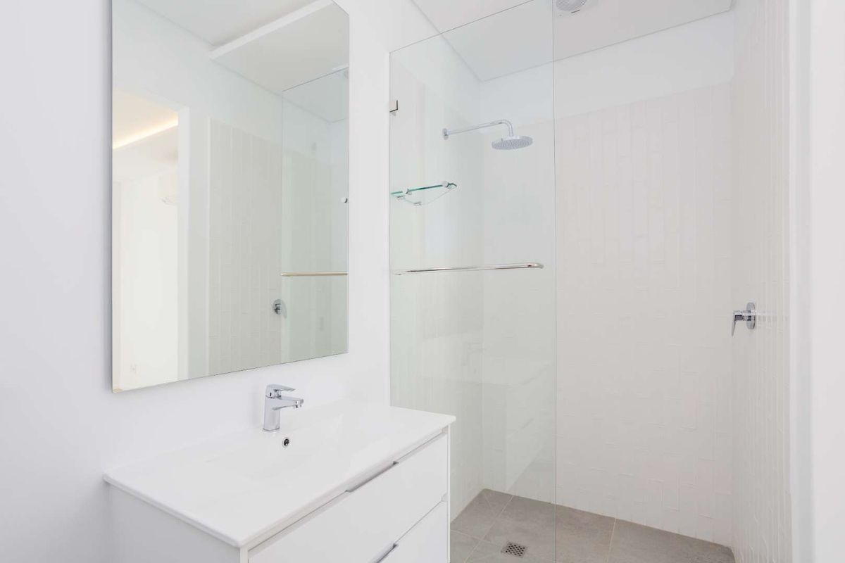Modern bathroom featuring a sleek white vanity, large wall mirror, and a spacious walk-in shower with a glass screen and rain shower head.