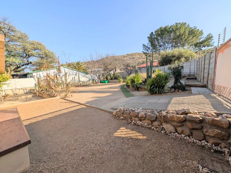 Spacious rear garden featuring a stone retaining wall, paved patio area, and secure boundary walls with electric fencing.