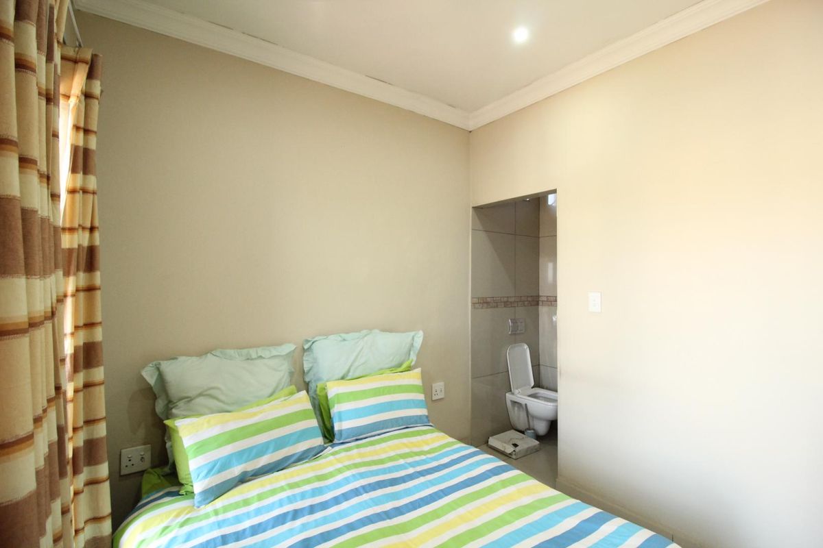 A bedroom featuring neutral wall tones, crown molding, and an en-suite bathroom with tiled finishes.