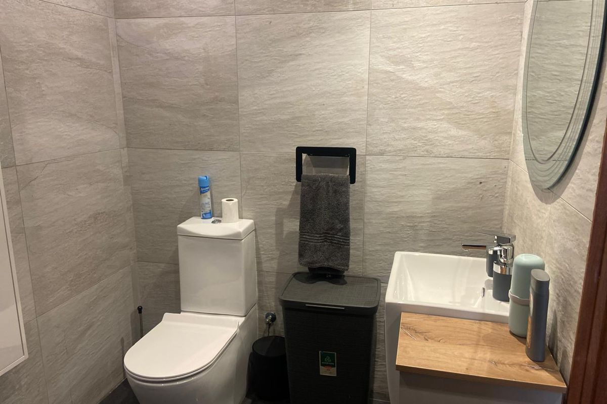 A modern guest bathroom featuring floor-to-ceiling stone-look wall tiles, a wall-mounted vanity with a basin, and a contemporary toilet.