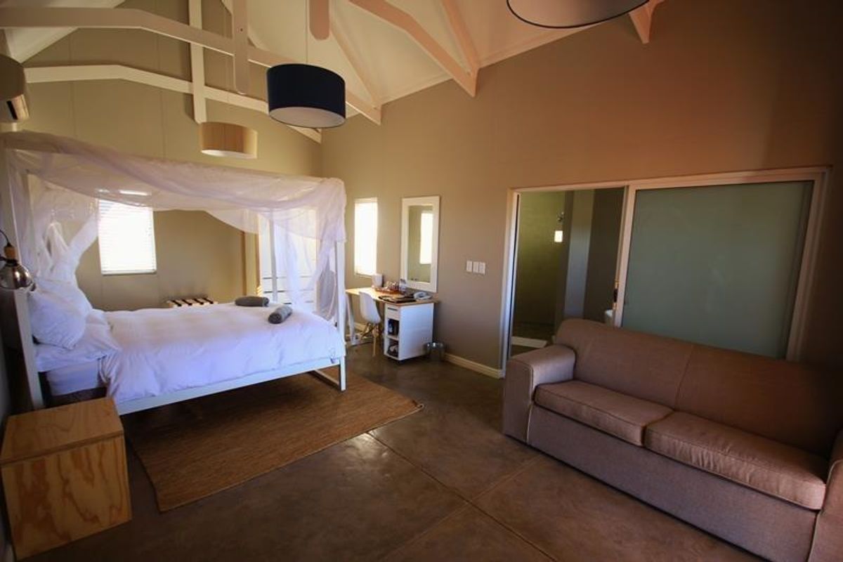 Spacious bedroom featuring vaulted ceilings with exposed rafters, polished concrete floors, and an en-suite bathroom access via a sliding door.