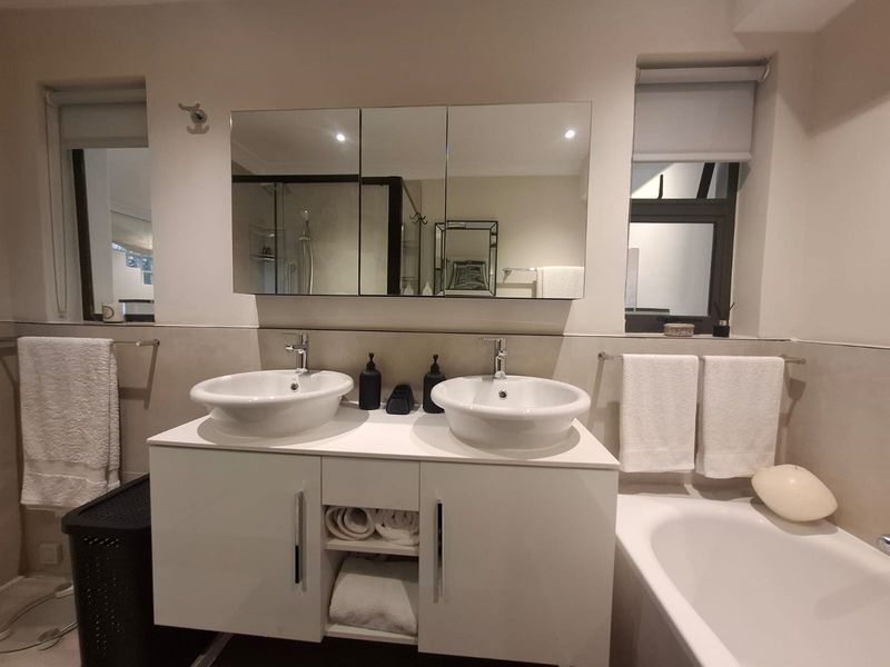 Modern bathroom featuring a double vanity with vessel sinks, a mirrored medicine cabinet, and a bathtub with neutral wall tiling.