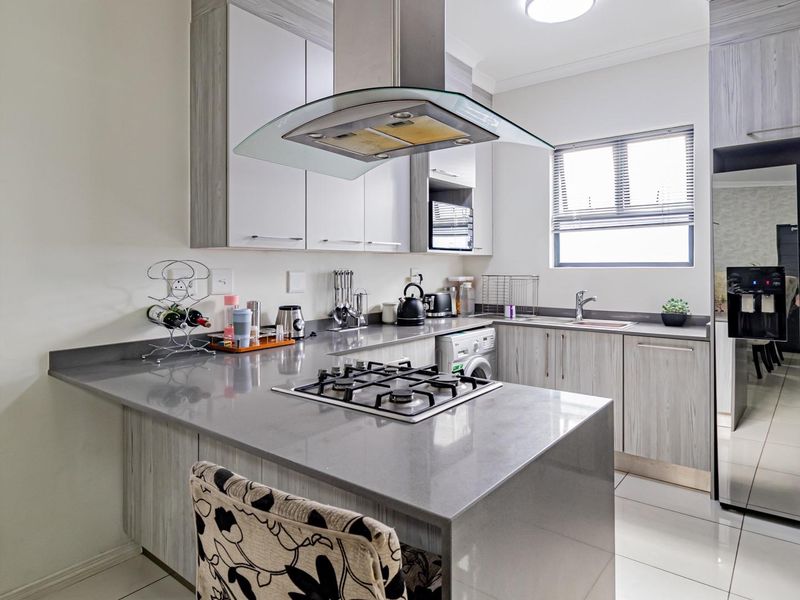 Modern kitchen featuring stone countertops, gas hob with extractor fan, and light wood-grain cabinetry, offering a functional and contemporary cooking space.