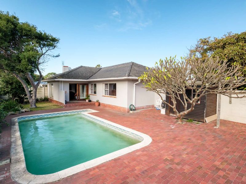 Rear exterior view featuring a swimming pool, brick paved patio area, and a detached timber garden shed set within a private backyard.