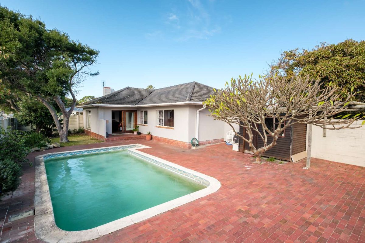 Rear exterior view featuring a swimming pool, brick paved patio area, and a detached timber garden shed set within a private backyard.