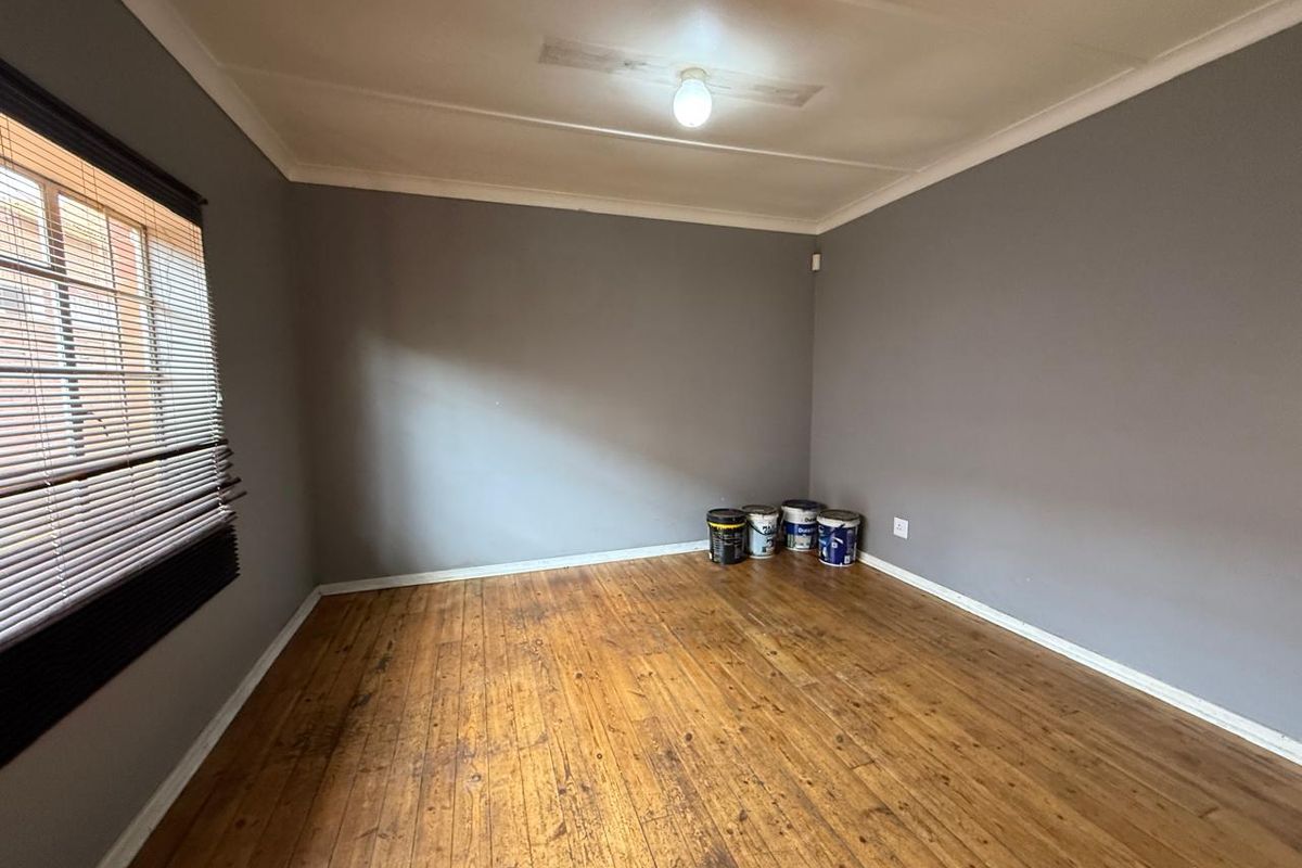 An empty bedroom featuring original timber flooring, grey painted walls, and venetian blinds, offering a blank canvas for personalization.