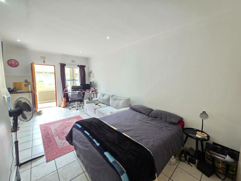 Open-plan studio apartment featuring tiled flooring, recessed lighting, and a kitchenette area with direct access to an outdoor balcony.