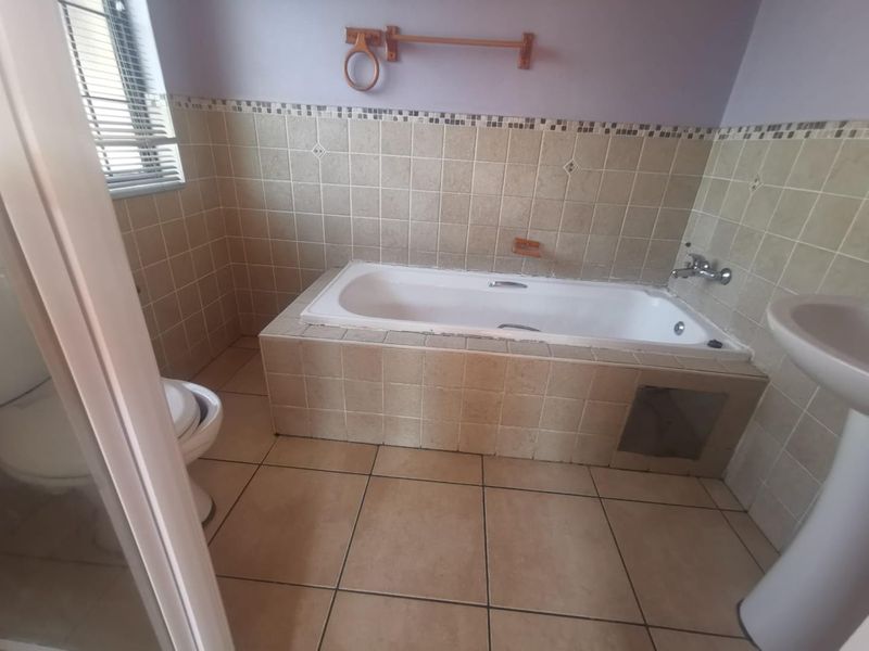 A dated bathroom featuring a built-in bathtub, pedestal basin, and toilet with neutral wall and floor tiling.