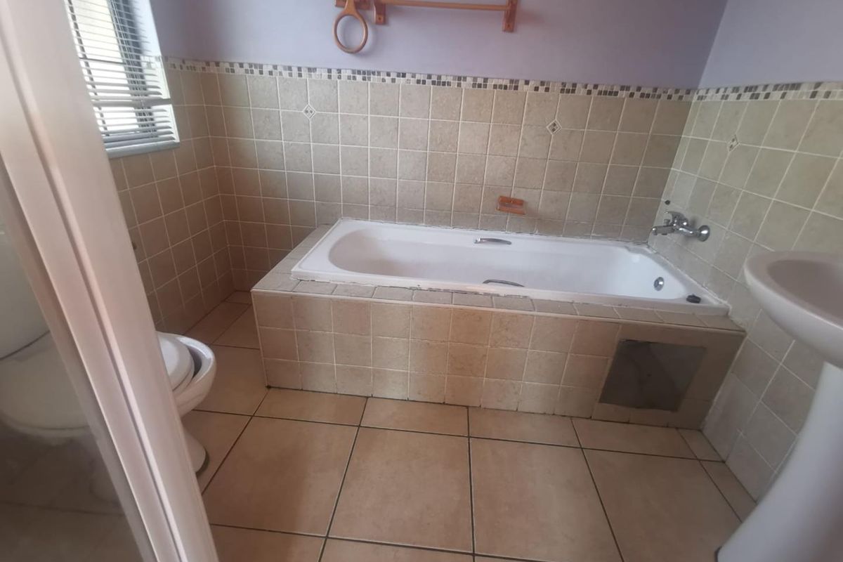 A dated bathroom featuring a built-in bathtub, pedestal basin, and toilet with neutral wall and floor tiling.