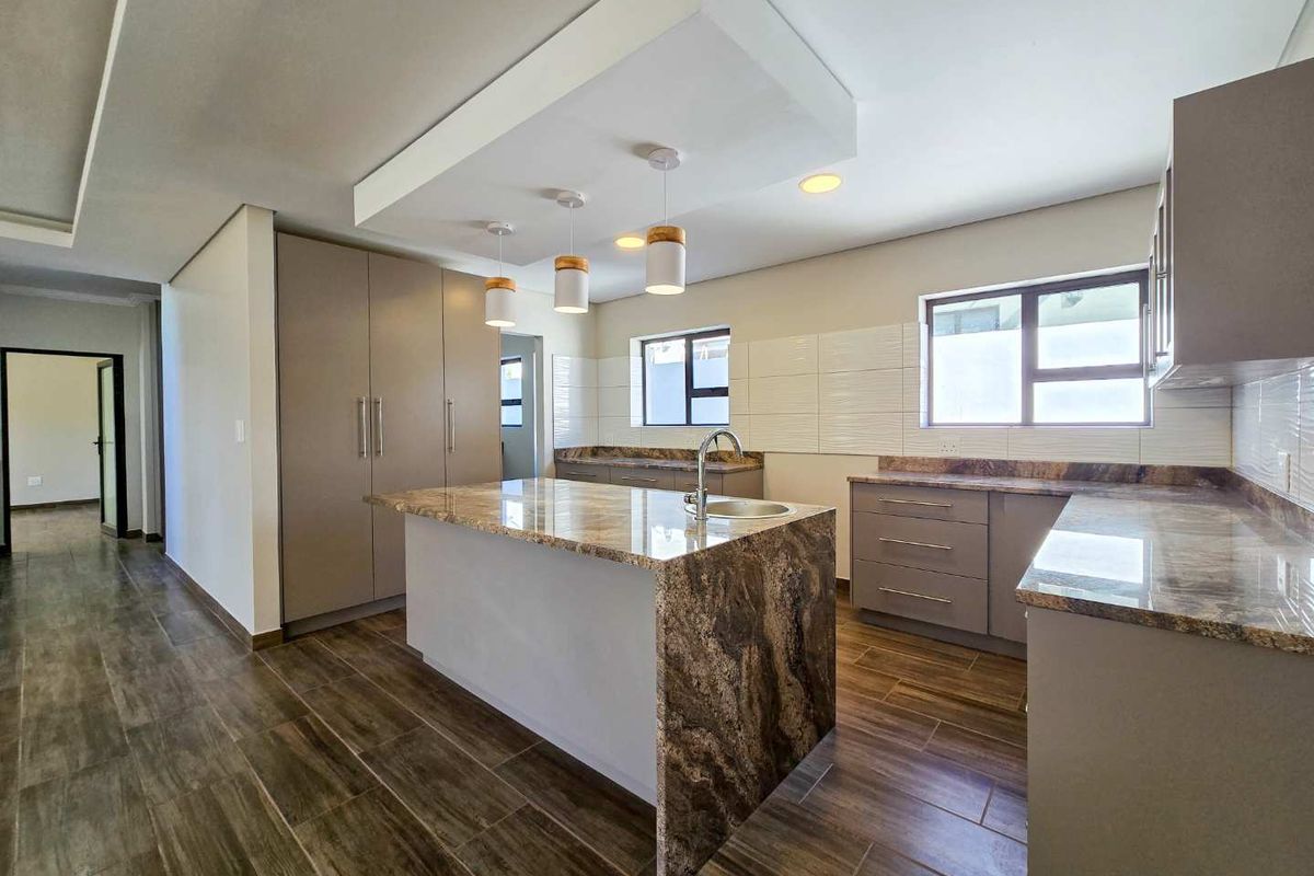 Modern kitchen featuring a central island with stone countertops, integrated cabinetry, tiled flooring, and a recessed ceiling detail with pendant lighting.