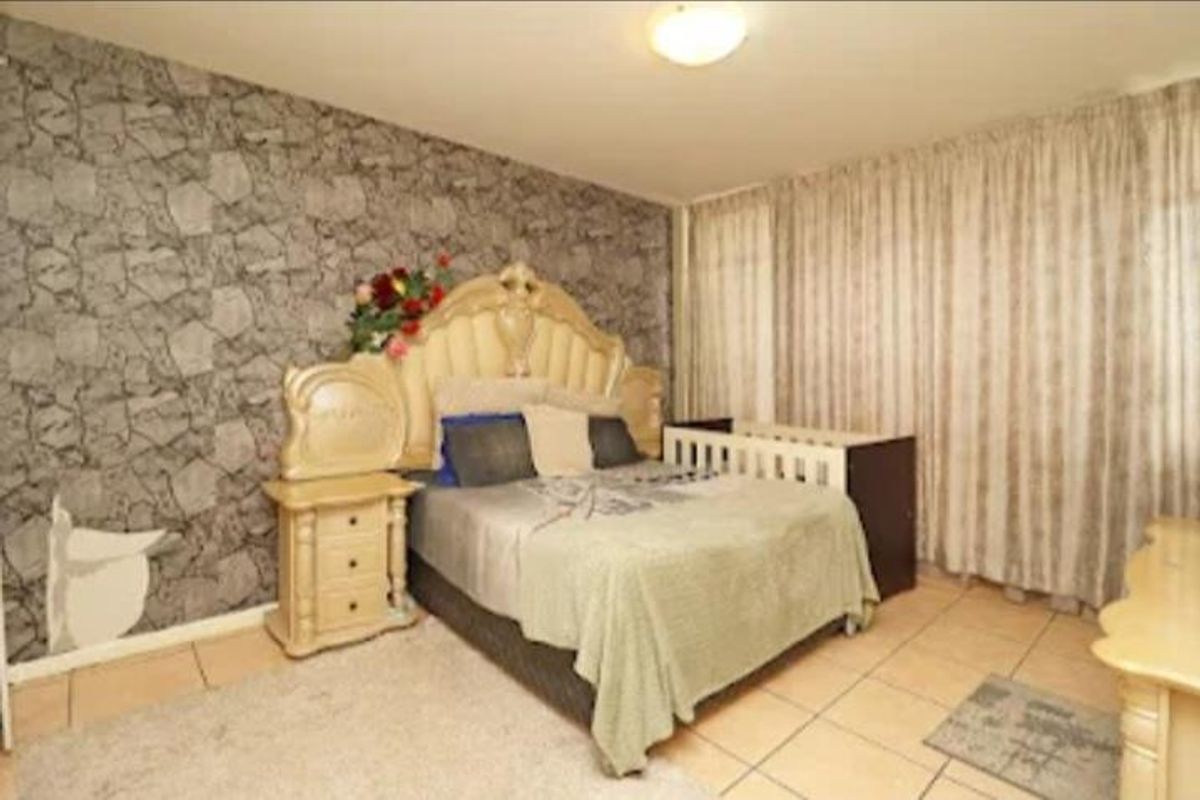 A bedroom featuring tiled flooring and a decorative feature wall with patterned wallpaper, offering a functional space with natural light through curtained windows.