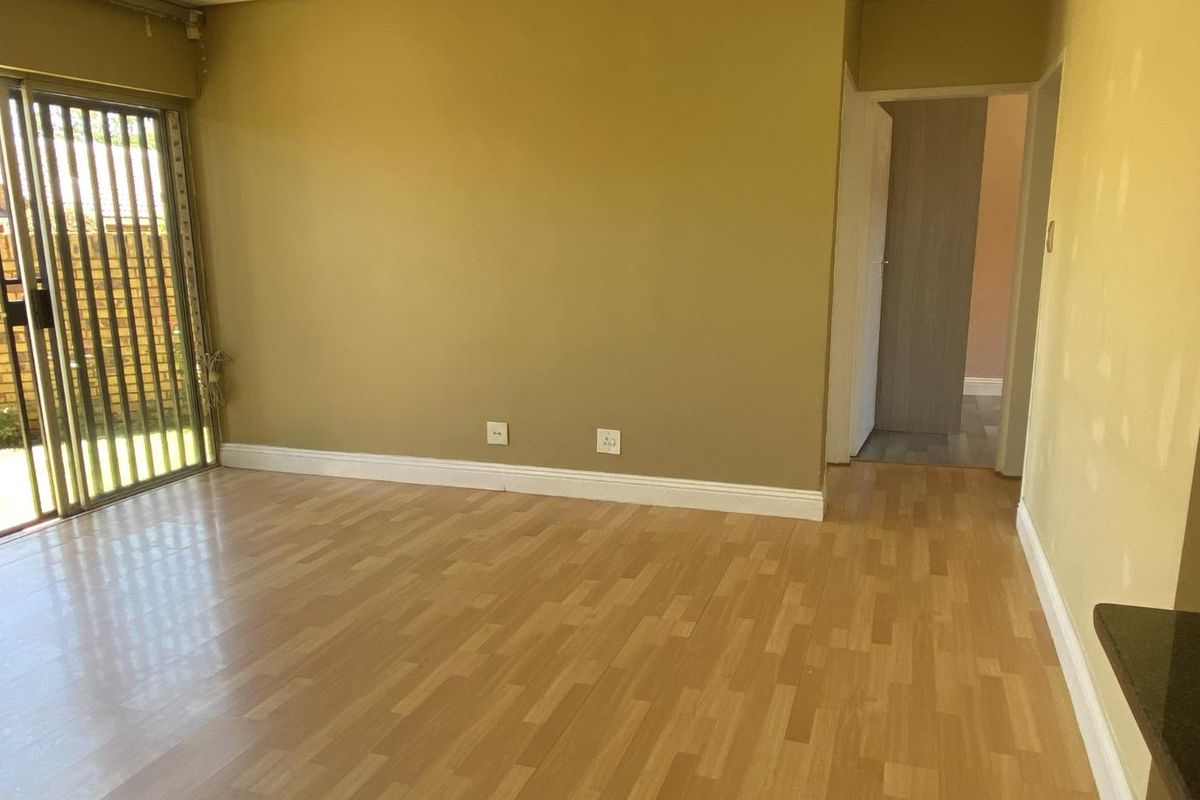 An empty living room featuring laminate flooring, recessed lighting, and a sliding glass door with a security gate leading to the exterior.
