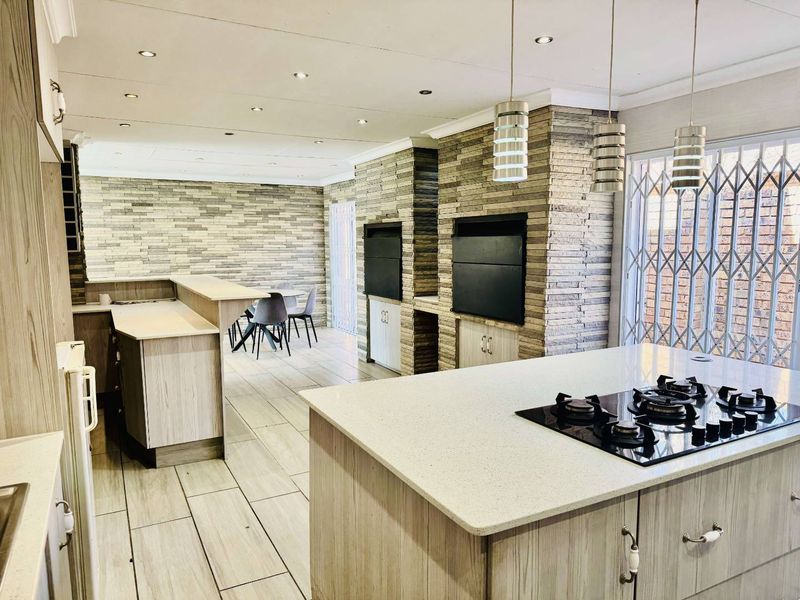 Spacious open-plan living area featuring a modern kitchen with island, gas hob, and a striking stone-clad feature wall with built-in braai facilities.