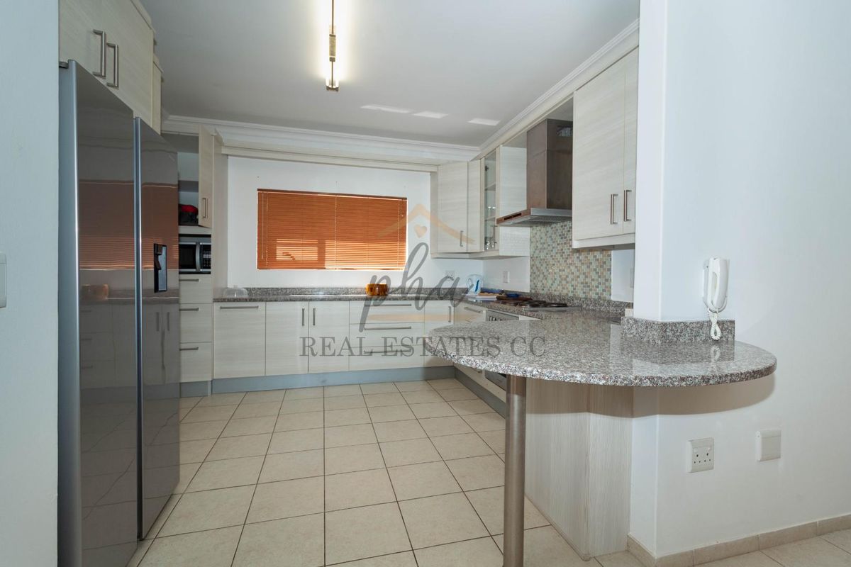 Modern kitchen featuring granite countertops, light wood cabinetry, tiled flooring, and a breakfast bar peninsula.