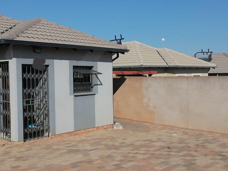 Rear exterior view of the house featuring a paved patio area, security gates, and a perimeter boundary wall.