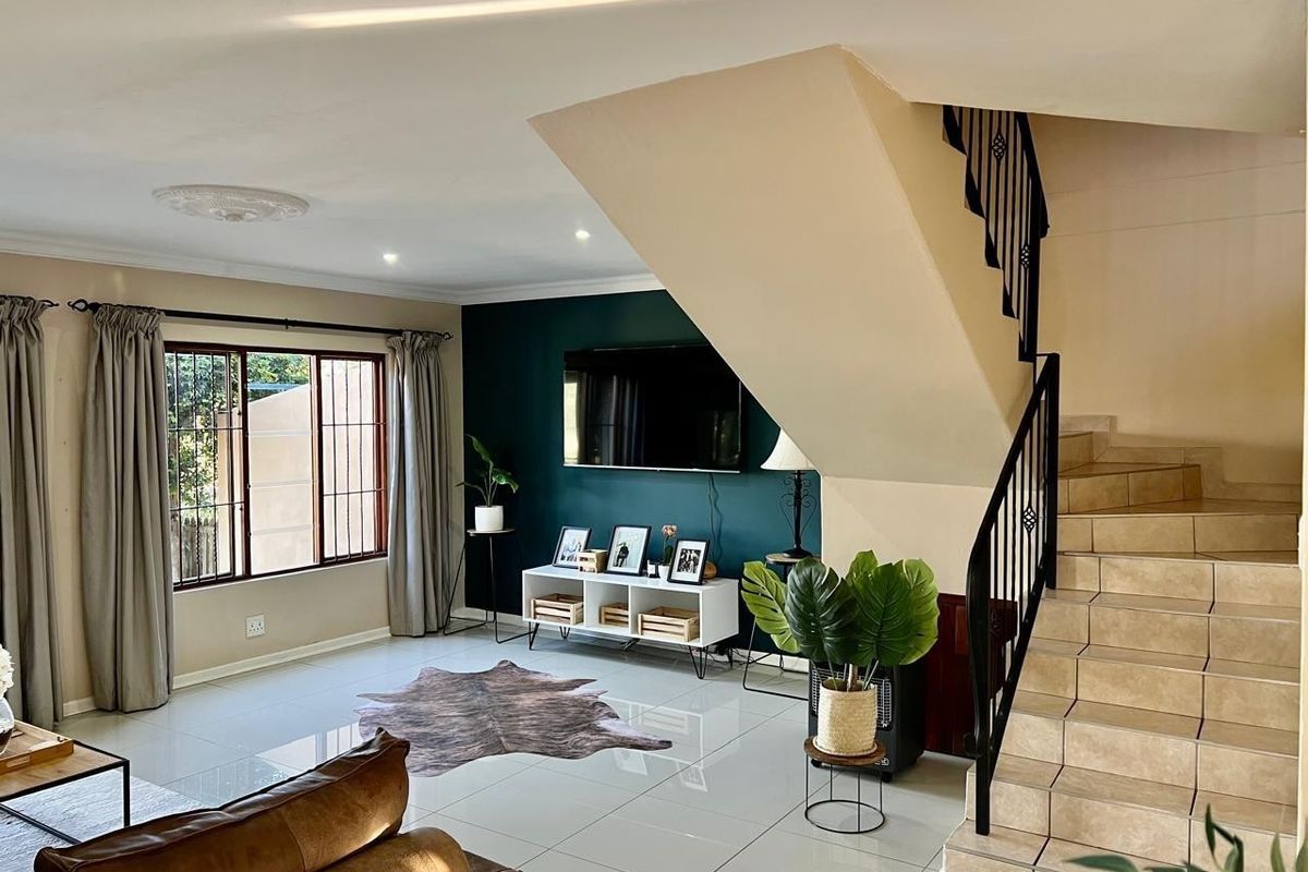 Spacious living room featuring polished tile flooring, a feature wall, and an internal staircase with a decorative metal balustrade.