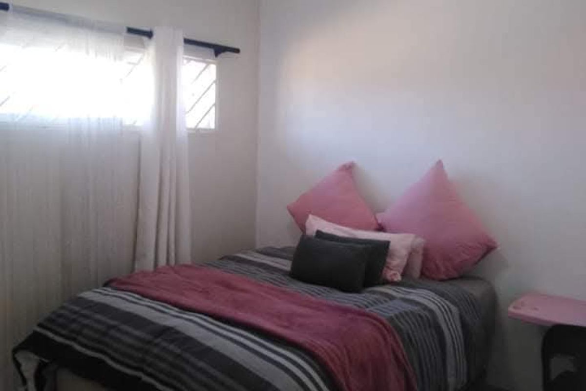 A functional bedroom featuring tiled flooring, a window with security bars, and a central ceiling light fixture.