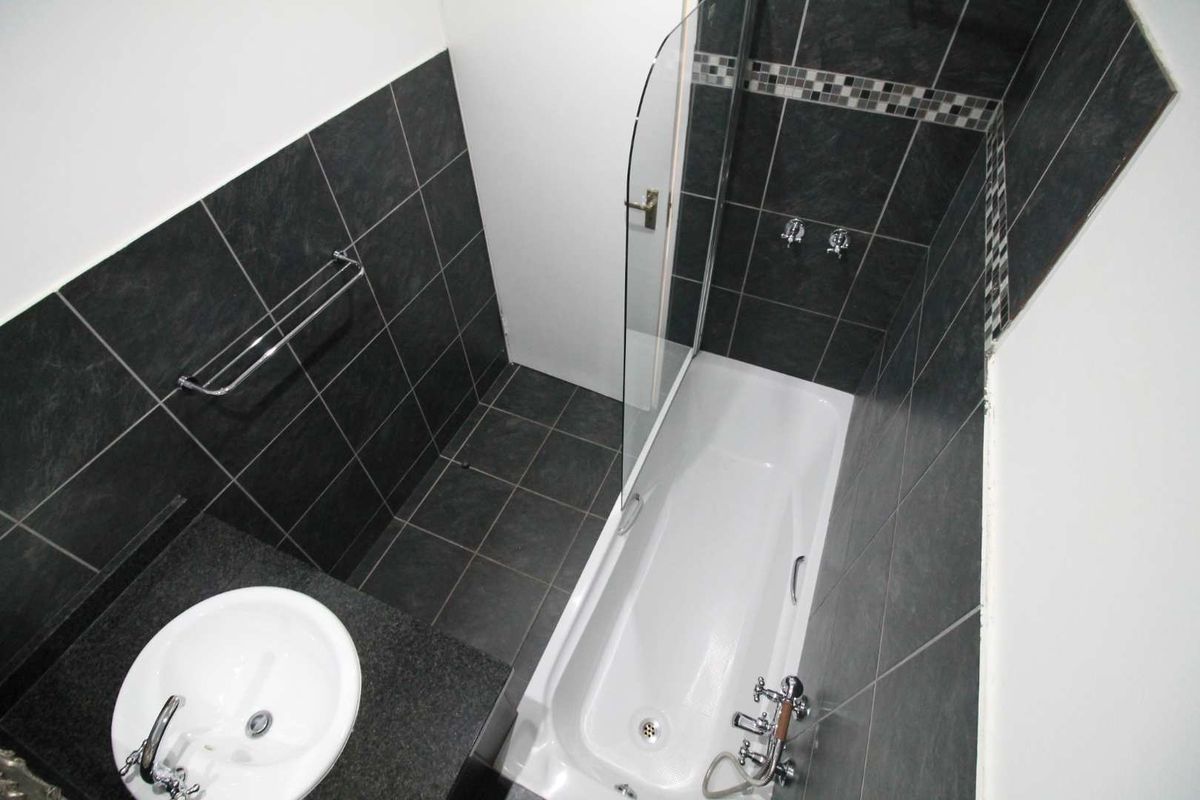 A modern bathroom featuring a bathtub with a glass shower screen, a vanity basin with a granite countertop, and dark tiled finishes.