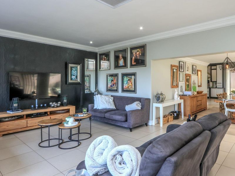 Spacious open-plan living and dining area featuring neutral tiled flooring, recessed lighting, crown molding, and a striking textured feature wall.