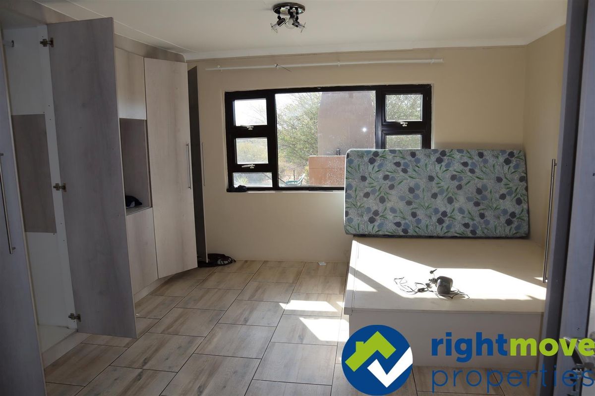A bedroom featuring light wood-look floor tiles, built-in cabinetry, and dark-framed windows providing natural light.
