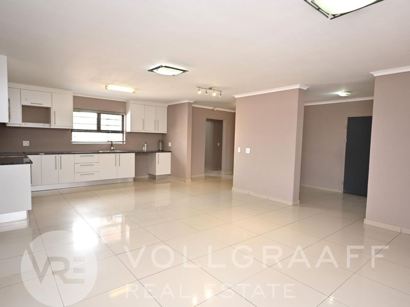 Spacious open-plan living area featuring a modern kitchen with white cabinetry, granite countertops, and large format floor tiles throughout.