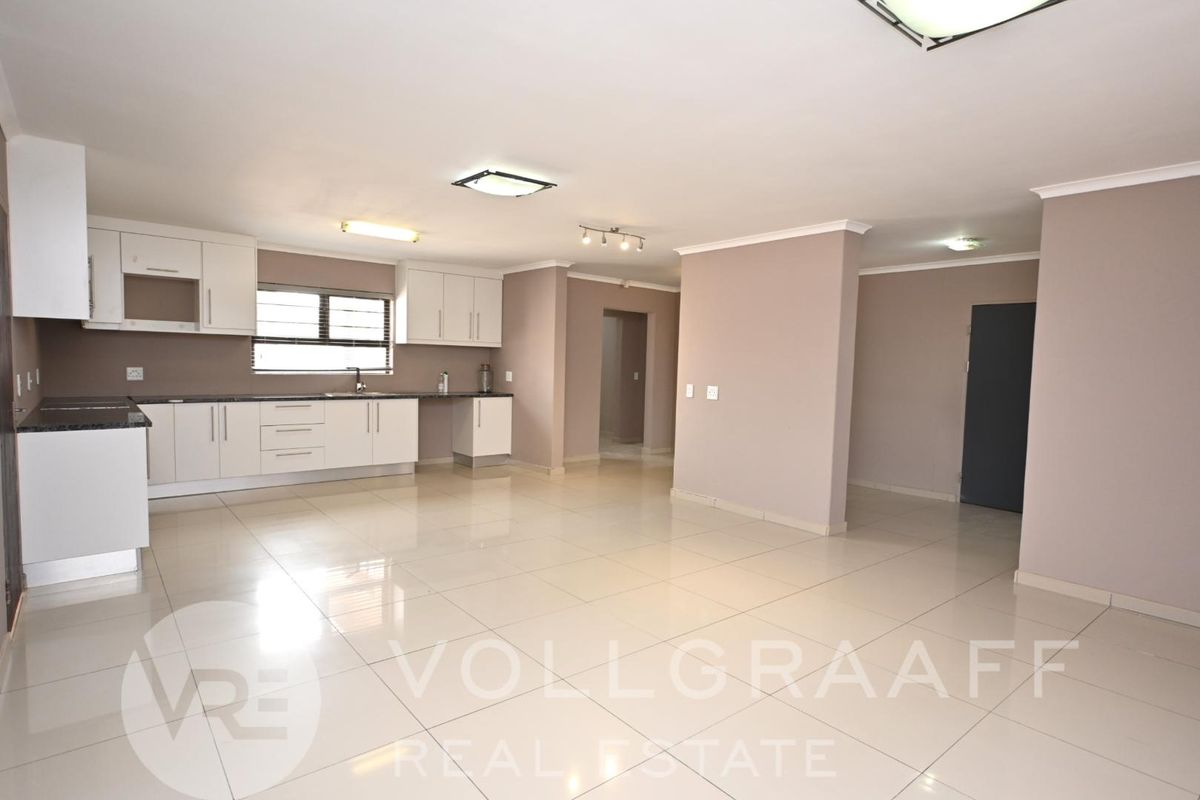 Spacious open-plan living area featuring a modern kitchen with white cabinetry, granite countertops, and large format floor tiles throughout.