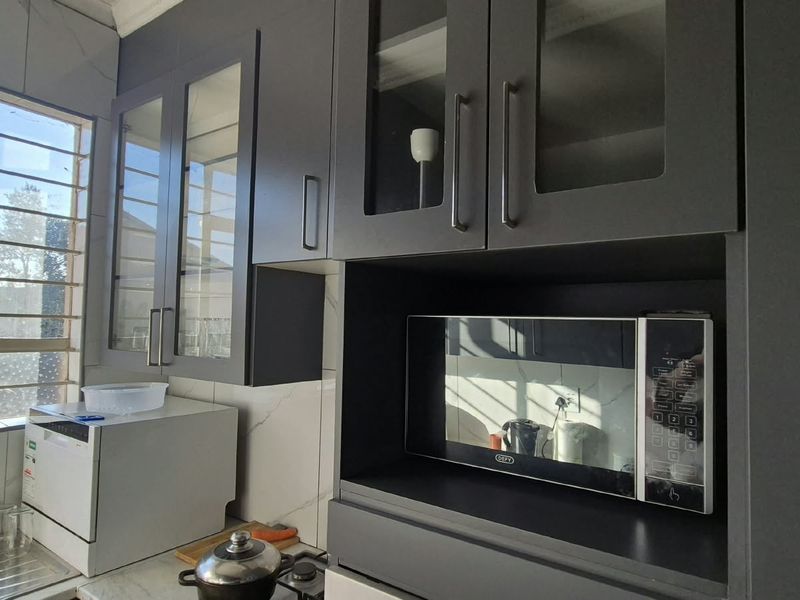 Modern kitchen area featuring dark grey cabinetry, glass-fronted display cupboards, built-in microwave, and marble-look wall tiling with natural light from the window.